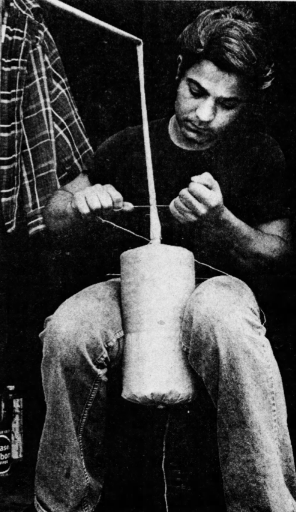 Nunzio Santore seated in 1973, tying string around a paper-wrapped shell held between his knees
