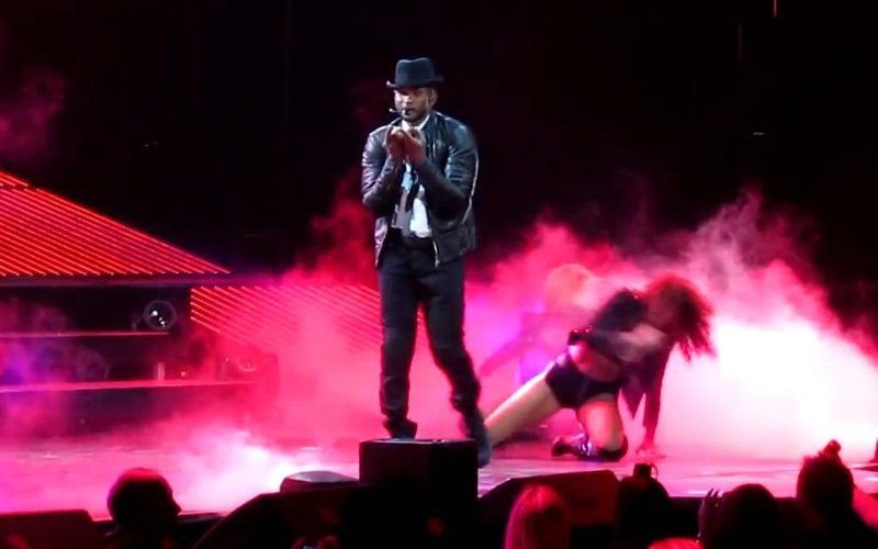 Performer in a hat and jacket on stage with a dancer, surrounded by pink-lit stage fog