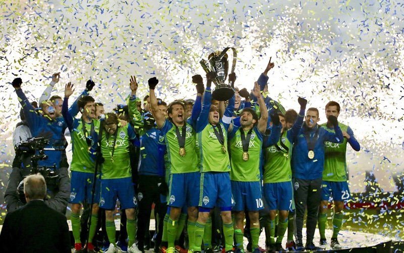 Soccer team lifting a trophy on the field as gold confetti fills the air above them