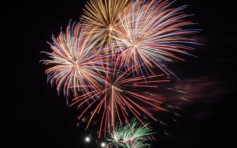 Gold, pink and blue fireworks bursting together against a black night sky