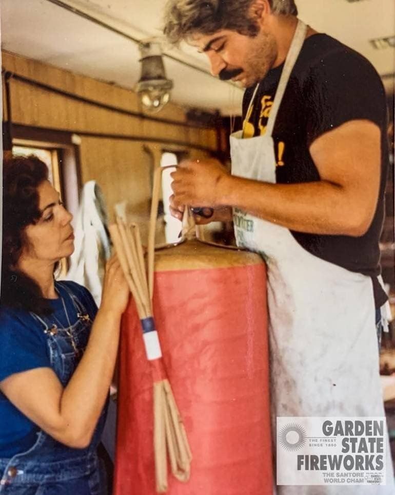 Frances and Nunzio Santore building a large red shell in the workshop, with a bundle of fuse sticks