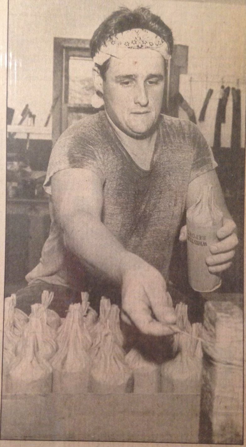 James Capozzoli in a bandana, reaching across a crate of wrapped finale shells in a newspaper print