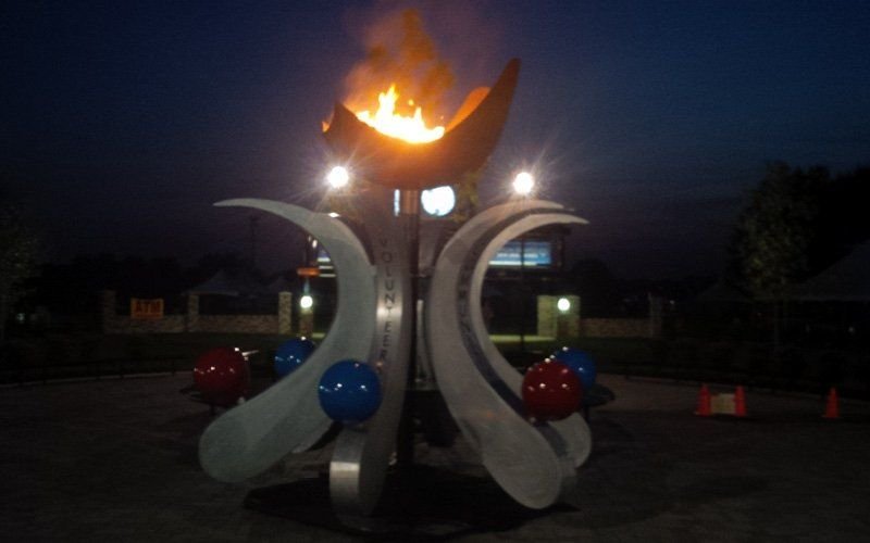 Lit ceremonial cauldron on a metal sculpture with red and blue spheres, outdoors at night