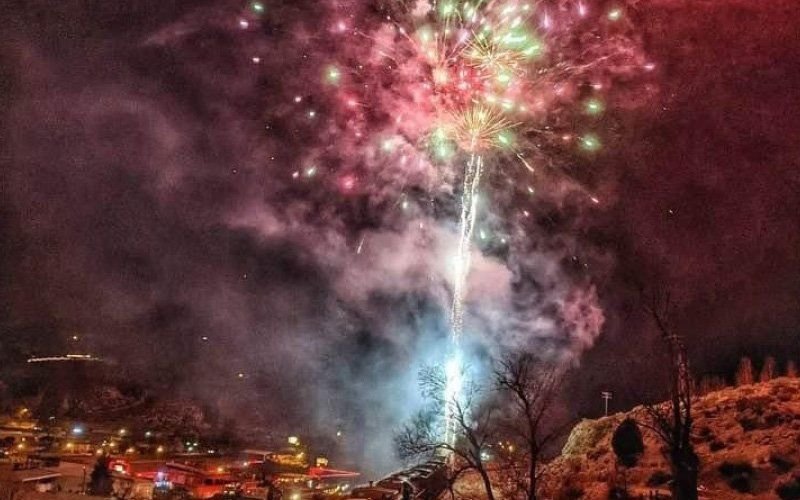 Pink and green fireworks and a white comet trail above a small hillside town at night