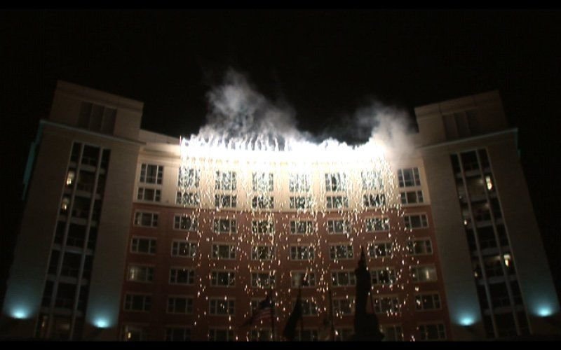 Sparks cascading down the face of a lit multi-story building like a waterfall at night